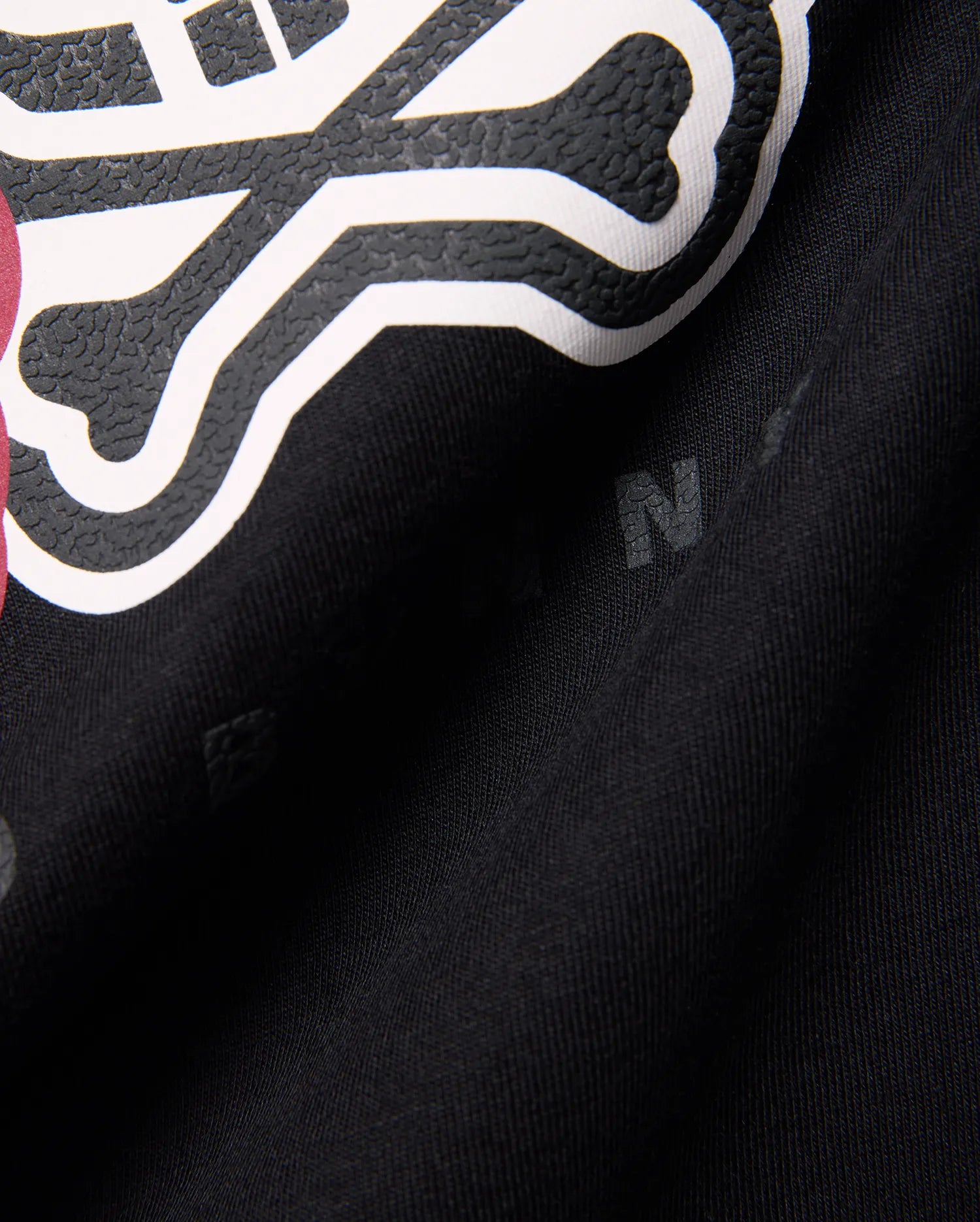 Kids Ledger Graphic Tee in black jersey knit, featuring a large, raised white and textured black Psycho Bunny skull graphic with a hint of dark pink, and subtle background letter prints.