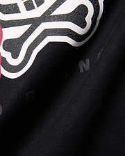 Kids Ledger Graphic Tee in black jersey knit, featuring a large, raised white and textured black Psycho Bunny skull graphic with a hint of dark pink, and subtle background letter prints.