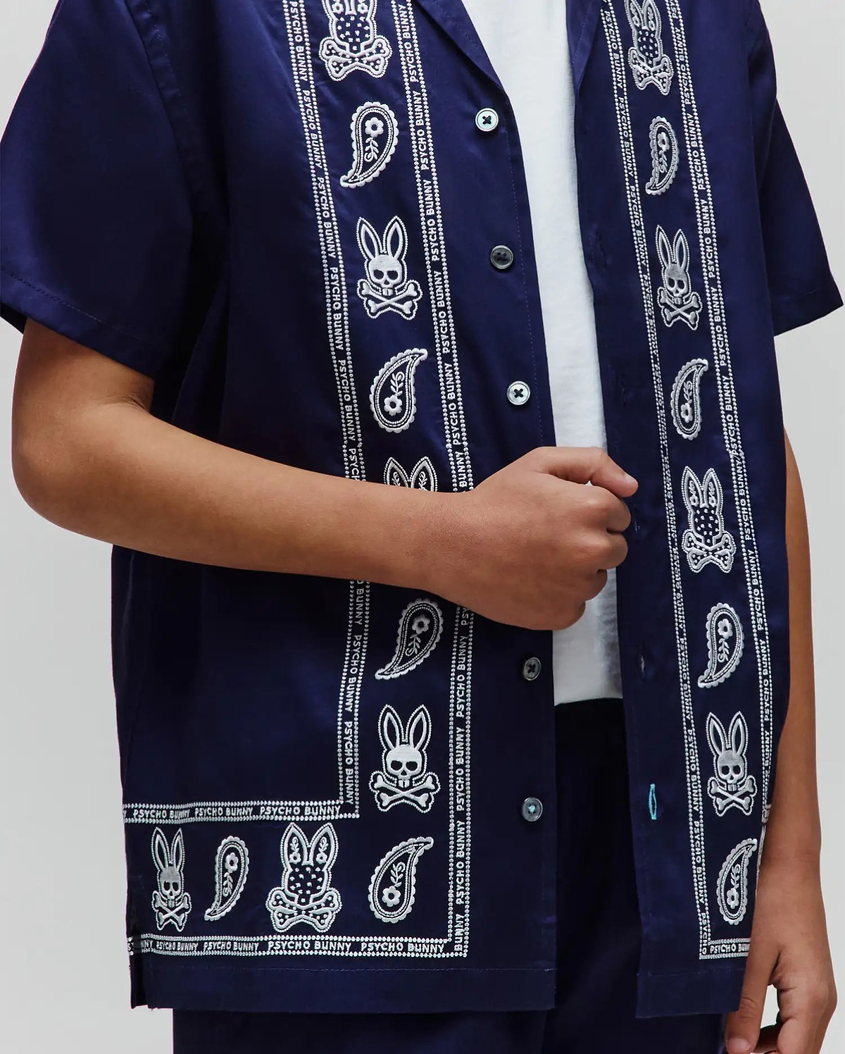 Kids Luke Tencel Border Shirt, a navy blue short-sleeve button-up with a white paisley and Psycho Bunny skull pattern border, featuring a relaxed fit and smooth fabric.