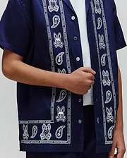 Kids Luke Tencel Border Shirt, a navy blue short-sleeve button-up with a white paisley and Psycho Bunny skull pattern border, featuring a relaxed fit and smooth fabric.