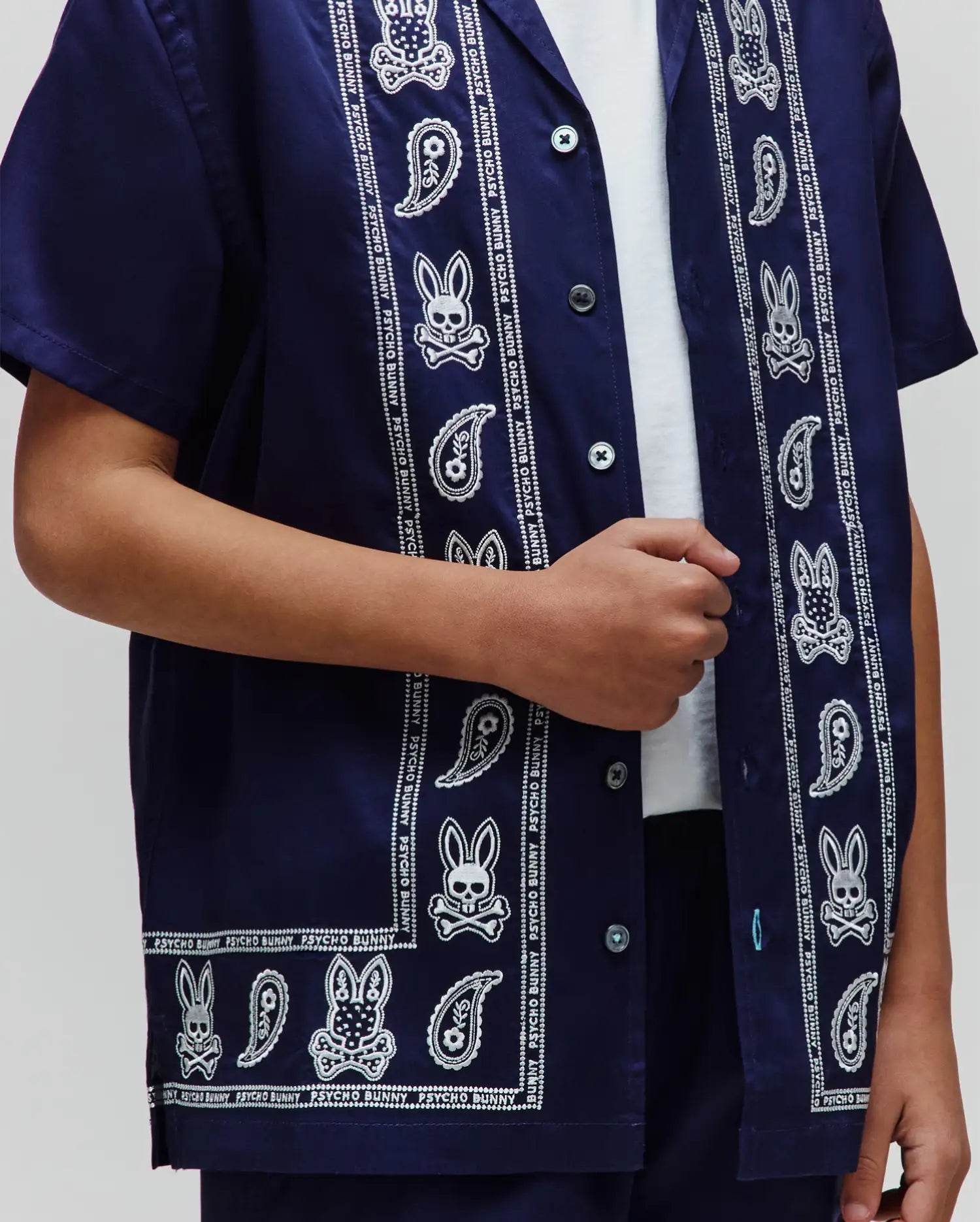 Kids Luke Tencel Border Shirt, a navy blue short-sleeve button-up with a white paisley and Psycho Bunny skull pattern border, featuring a relaxed fit and smooth fabric.