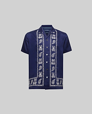 Kids Luke Tencel Border Shirt, a navy blue relaxed fit short-sleeve shirt in smooth Tencel. Features white vertical Psycho Bunny skull and paisley border patterns on the placket and hem, with a small embroidered chest logo.