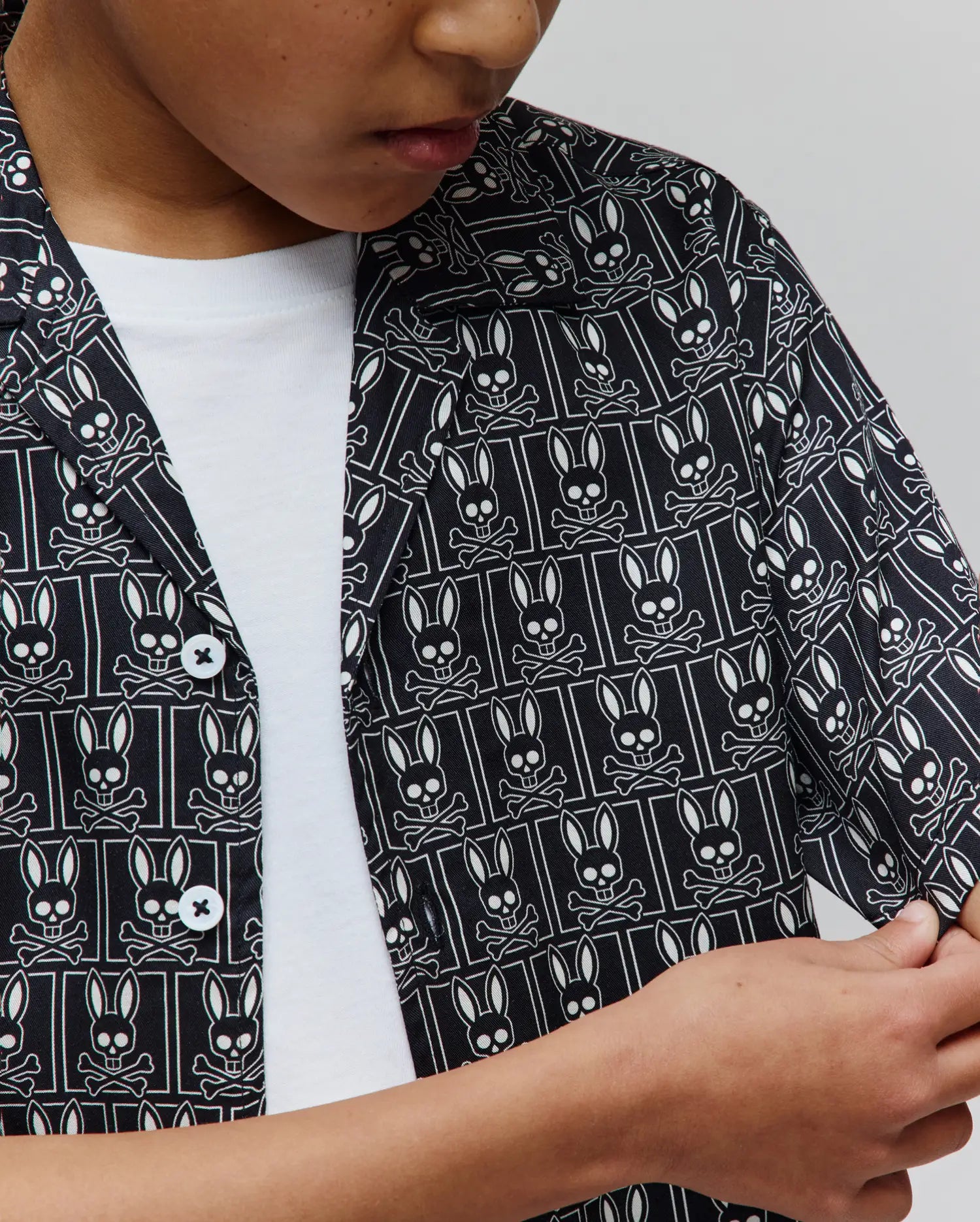 Kids Keon Tencel Shirt, a black short-sleeve woven shirt featuring a classic fit and an all-over white Psycho Bunny skull and crossbones logo pattern, complete with white buttons.
