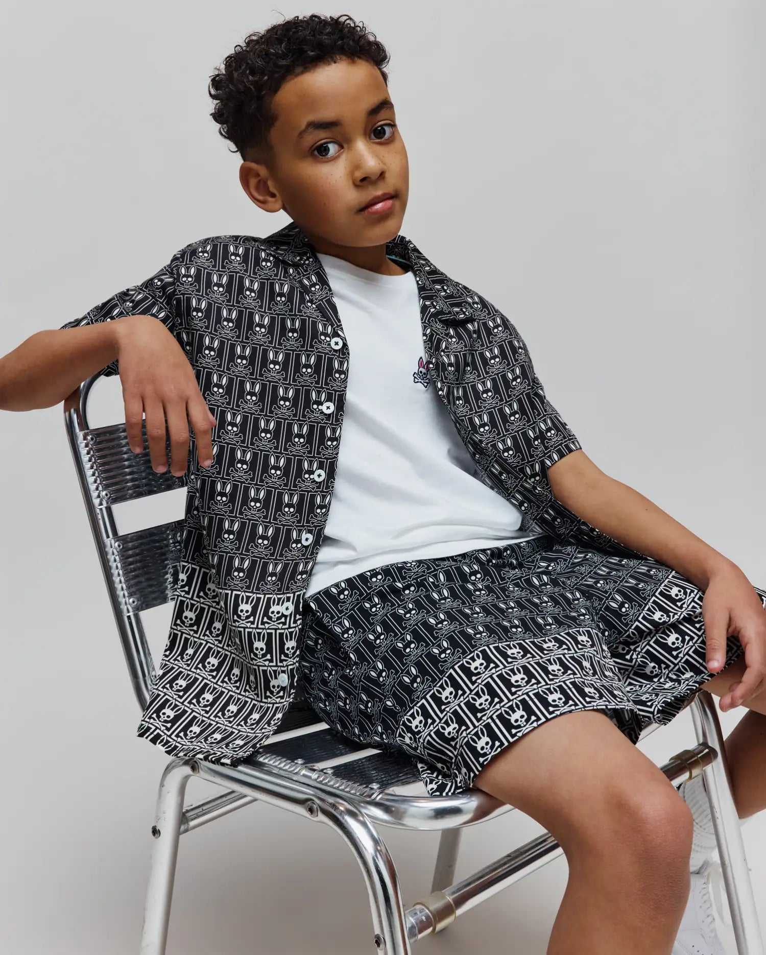 Kids Keon Tencel Shirt, a black and white allover Psycho Bunny skull grid patterned short-sleeve shirt, paired with matching shorts and a white tee with small colorful chest logo.