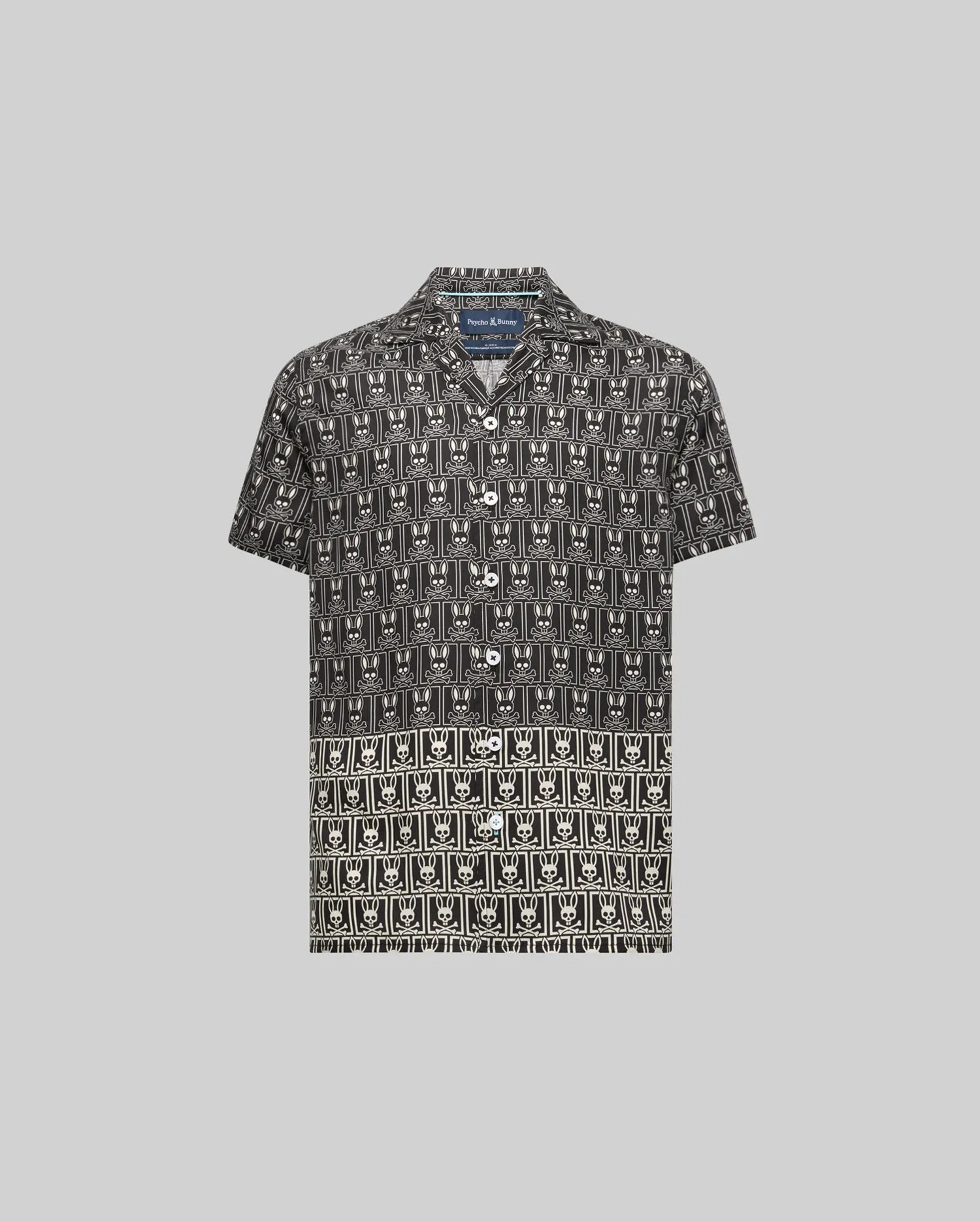 Kids Keon Tencel Shirt, a relaxed fit black short-sleeve button-up with an all-over white Psycho Bunny skull logo pattern, featuring a distinct two-tone design and white buttons.