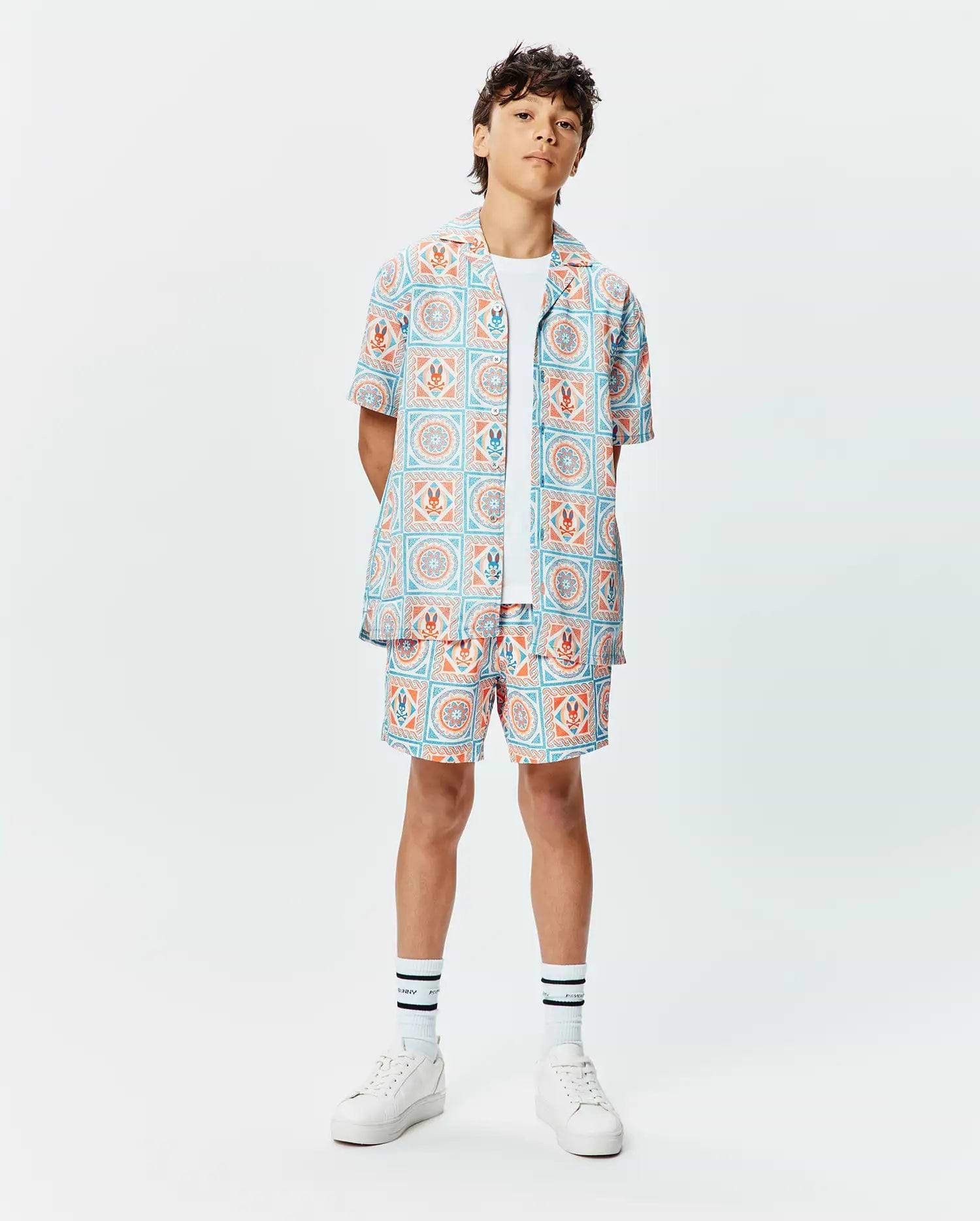 Kids Frank Tencel Shirt and matching relaxed-fit shorts, featuring a vibrant light blue and orange tiled geometric pattern with integrated Psycho Bunny skull logos throughout.