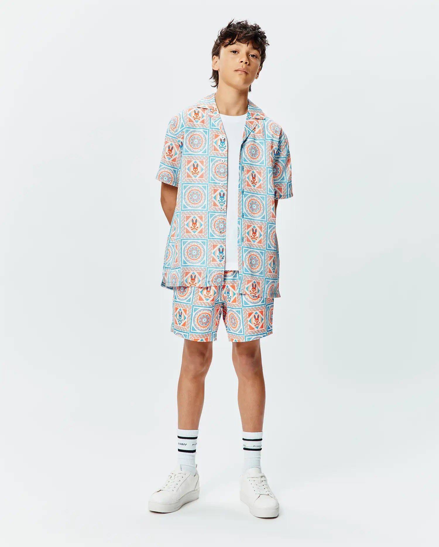 Kids Frank Tencel Shirt and matching relaxed-fit shorts, featuring a vibrant light blue and orange tiled geometric pattern with integrated Psycho Bunny skull logos throughout.
