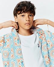 Kids Frank Tencel Shirt, a relaxed fit short-sleeve button-up in white with blue and orange mosaic bunny skull pattern, worn over a classic white jersey t-shirt with a small embroidered Psycho Bunny logo on the left chest.