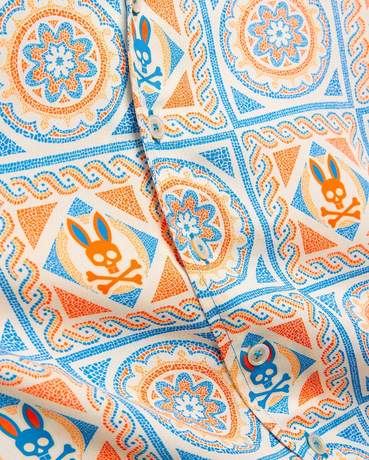 Kids Frank Tencel Shirt in cream with an all-over vibrant blue and orange mosaic pattern featuring repeated Psycho Bunny skull logos and intricate floral designs on smooth Tencel fabric.