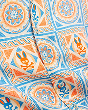 Kids Frank Tencel Shirt in cream with an all-over vibrant blue and orange mosaic pattern featuring repeated Psycho Bunny skull logos and intricate floral designs on smooth Tencel fabric.