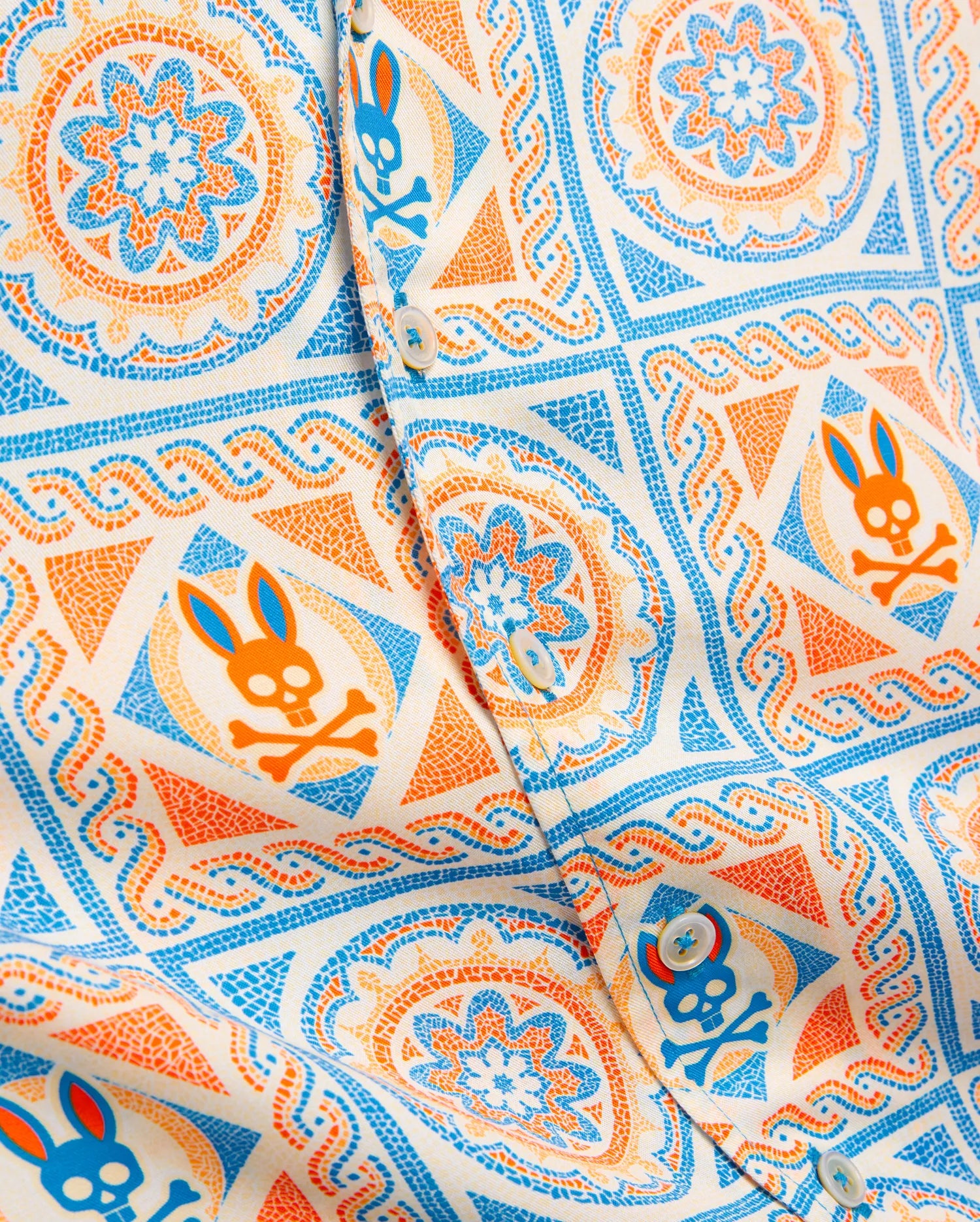 Kids Frank Tencel Shirt in cream with an all-over vibrant blue and orange mosaic pattern featuring repeated Psycho Bunny skull logos and intricate floral designs on smooth Tencel fabric.