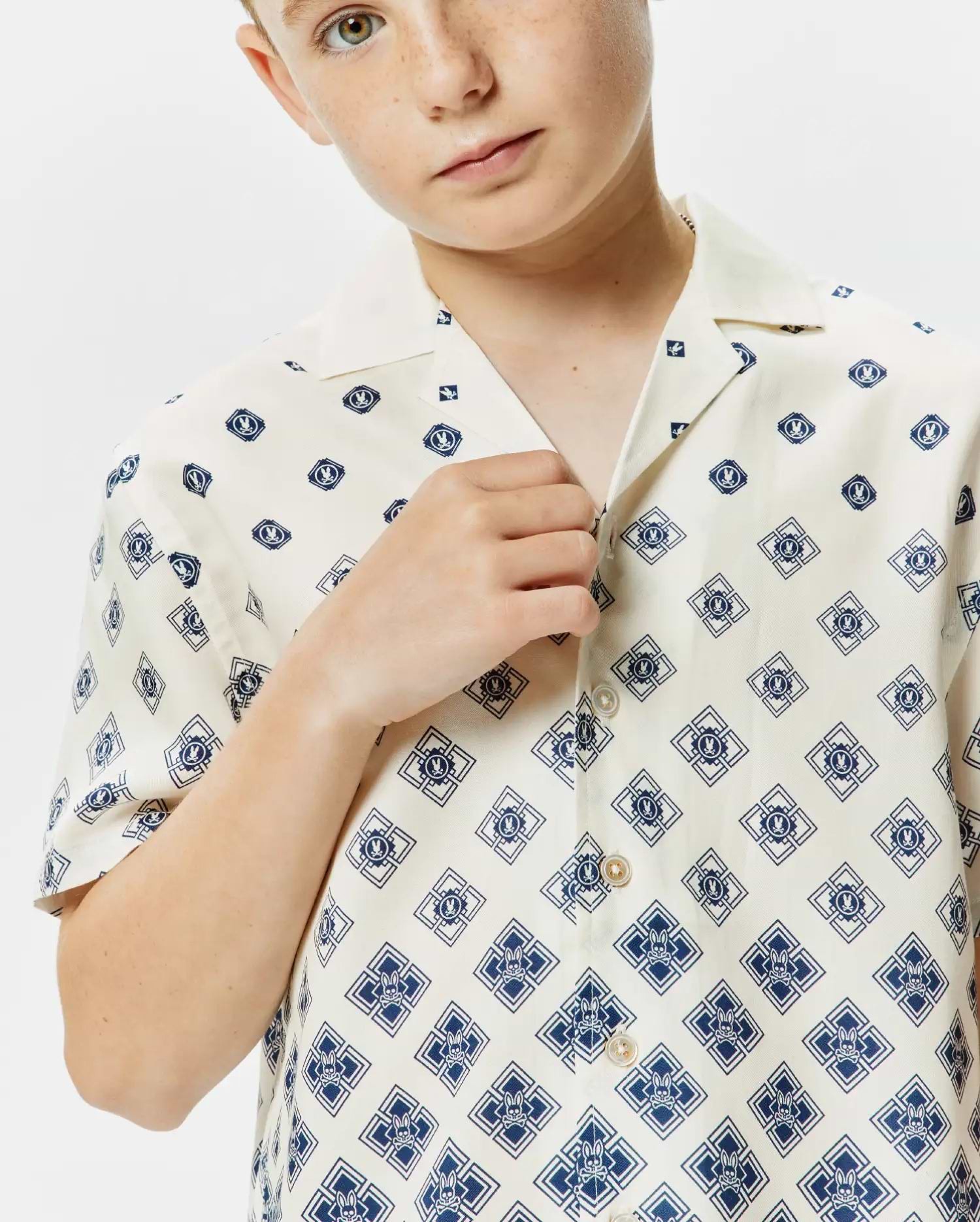 KIDS TOBIAS TENCEL SHIRT: Cream short-sleeve camp collar shirt with an all-over navy diamond pattern featuring the iconic Psycho Bunny skull logo, classic fit, smooth Tencel fabric.