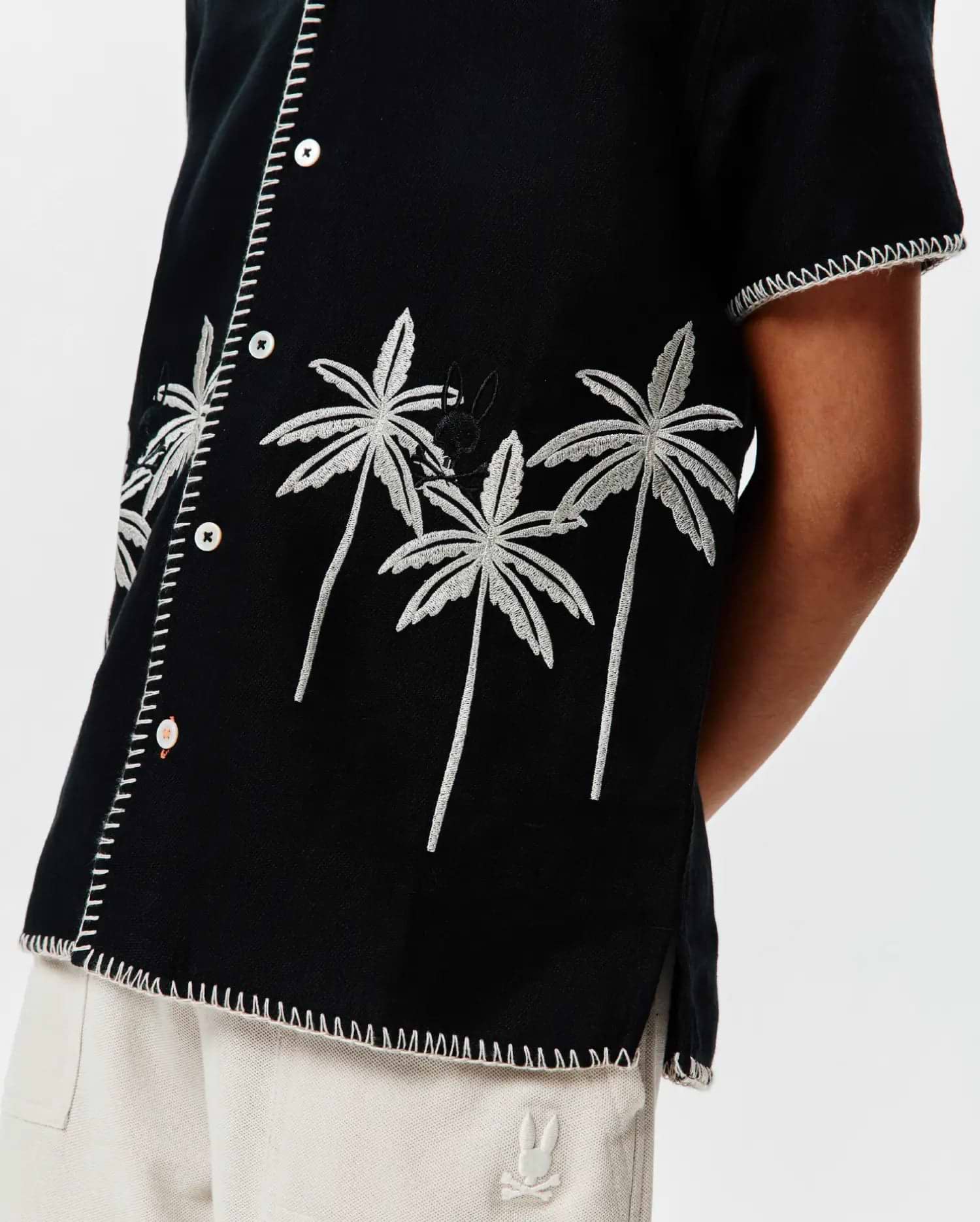 Kids Brad Linen Shirt: Black relaxed-fit linen shirt featuring white embroidered palm trees, a subtle black Psycho Bunny skull logo, and decorative white stitching along the placket, sleeves, and hem.