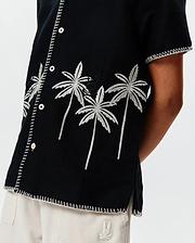 Kids Brad Linen Shirt: Black relaxed-fit linen shirt featuring white embroidered palm trees, a subtle black Psycho Bunny skull logo, and decorative white stitching along the placket, sleeves, and hem.