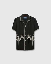 Kids Brad Linen Shirt, black relaxed fit with white contrast stitching, white buttons, and cream embroidered palm trees featuring a small Psycho Bunny skull logo on the lower front.