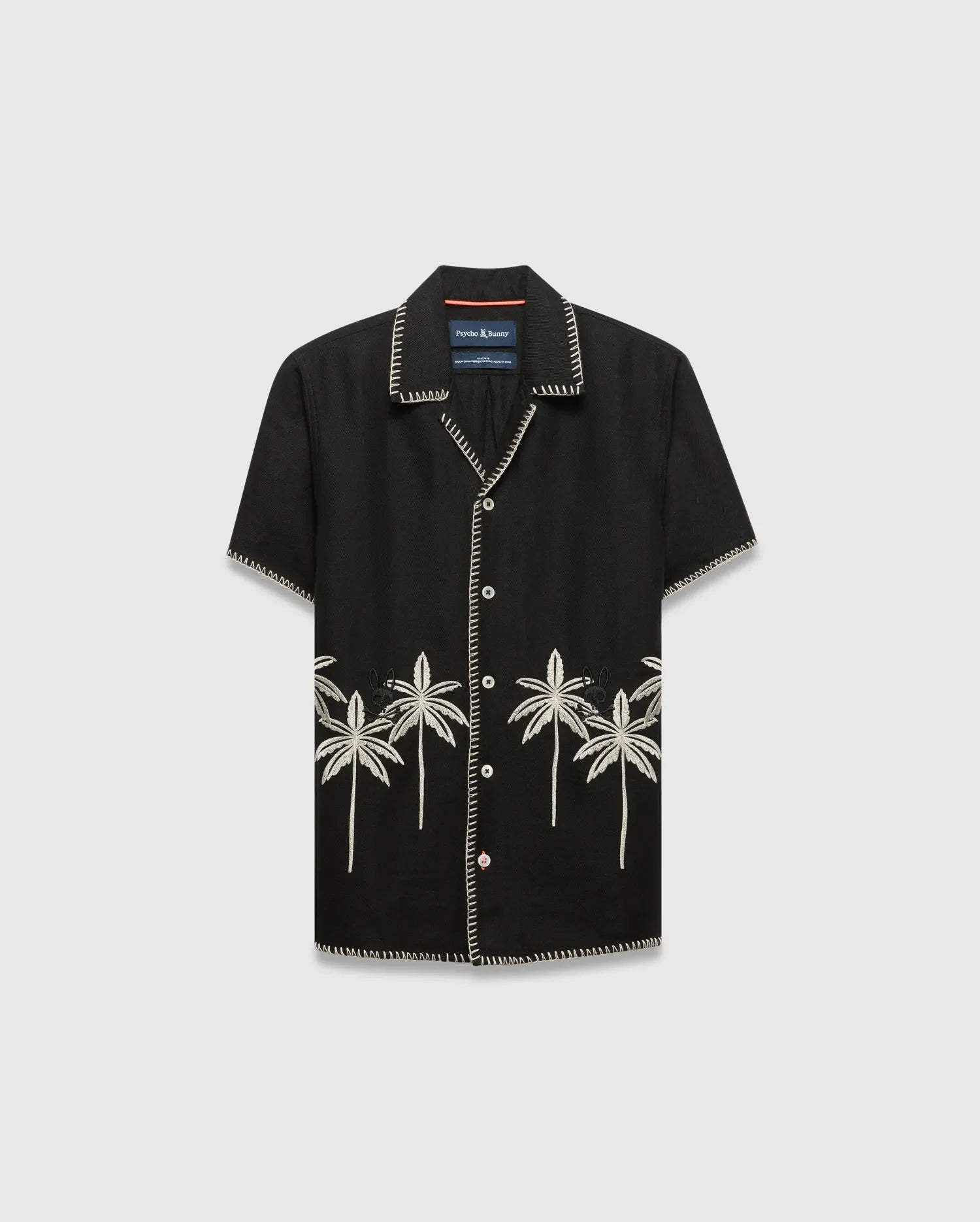 Kids Brad Linen Shirt, black relaxed fit with white contrast stitching, white buttons, and cream embroidered palm trees featuring a small Psycho Bunny skull logo on the lower front.