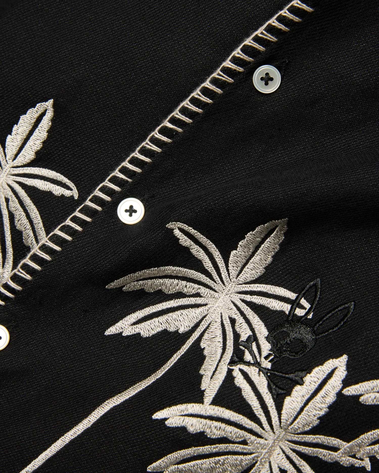 Kids Brad Linen Shirt, black with intricate off-white embroidered palm trees, a small black Psycho Bunny skull logo, and decorative zigzag placket stitching.