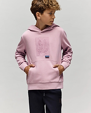 A young boy wears the KIDS GRANT HOODIE - KT0500020 by Psycho Bunny in light purple, made from a premium cotton blend with an embroidered Bunny skull and crossbones, standing with hands in the pocket against a plain background.