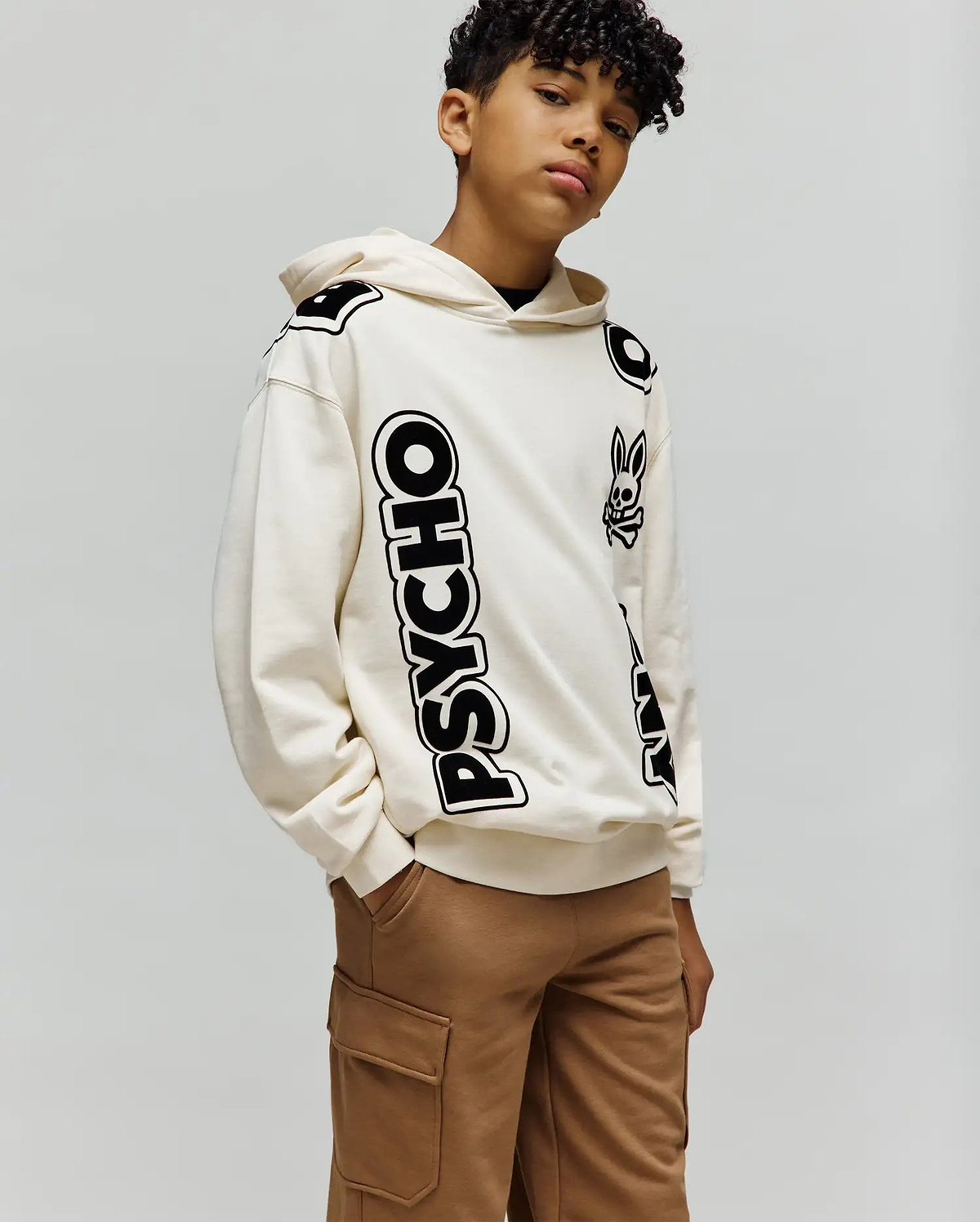 Kids Toby Oversized Hoodie in cream, featuring a bold vertical black PSYCHO text graphic and scattered black Psycho Bunny skull logos, crafted from a soft cotton blend.