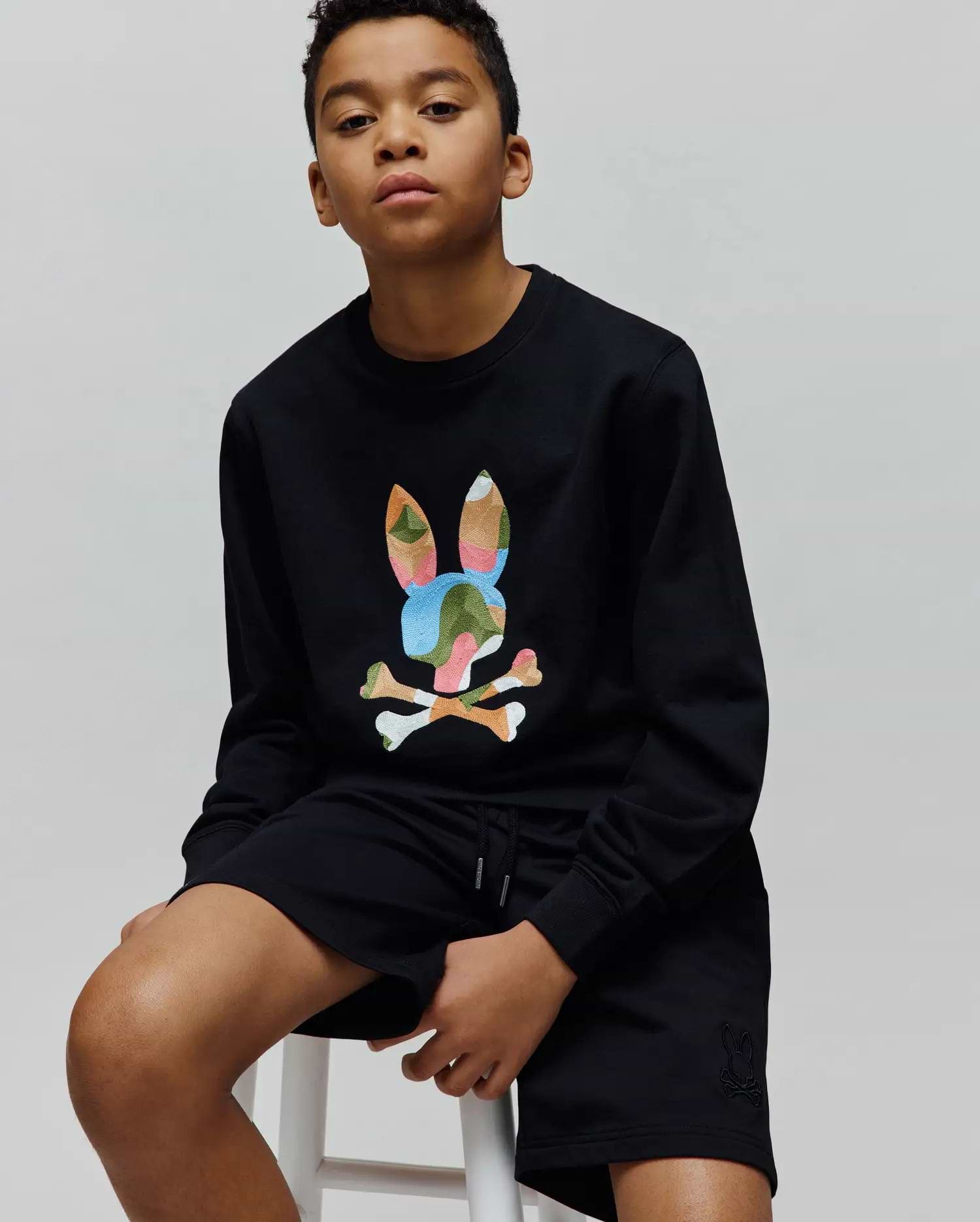 Black Kids Ara Crew sweatshirt with a large multicolor camo embroidered Psycho Bunny skull on the chest, paired with black shorts featuring a small tonal embroidered bunny skull on the left leg.