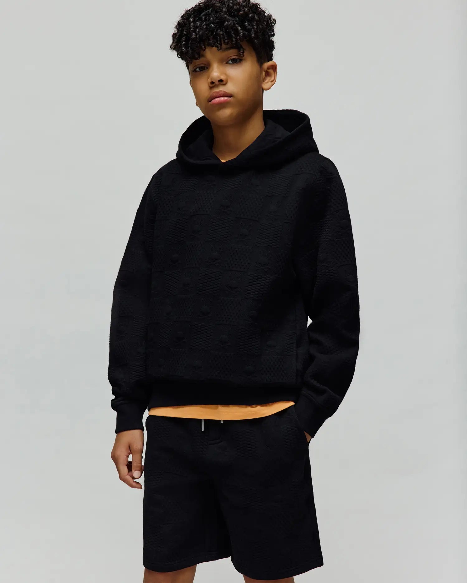 Kids Dustin Hoodie, a black relaxed fit hoodie featuring an all-over embossed Psycho Bunny skull pattern on textured knit fabric, with a subtle orange accent. (4)