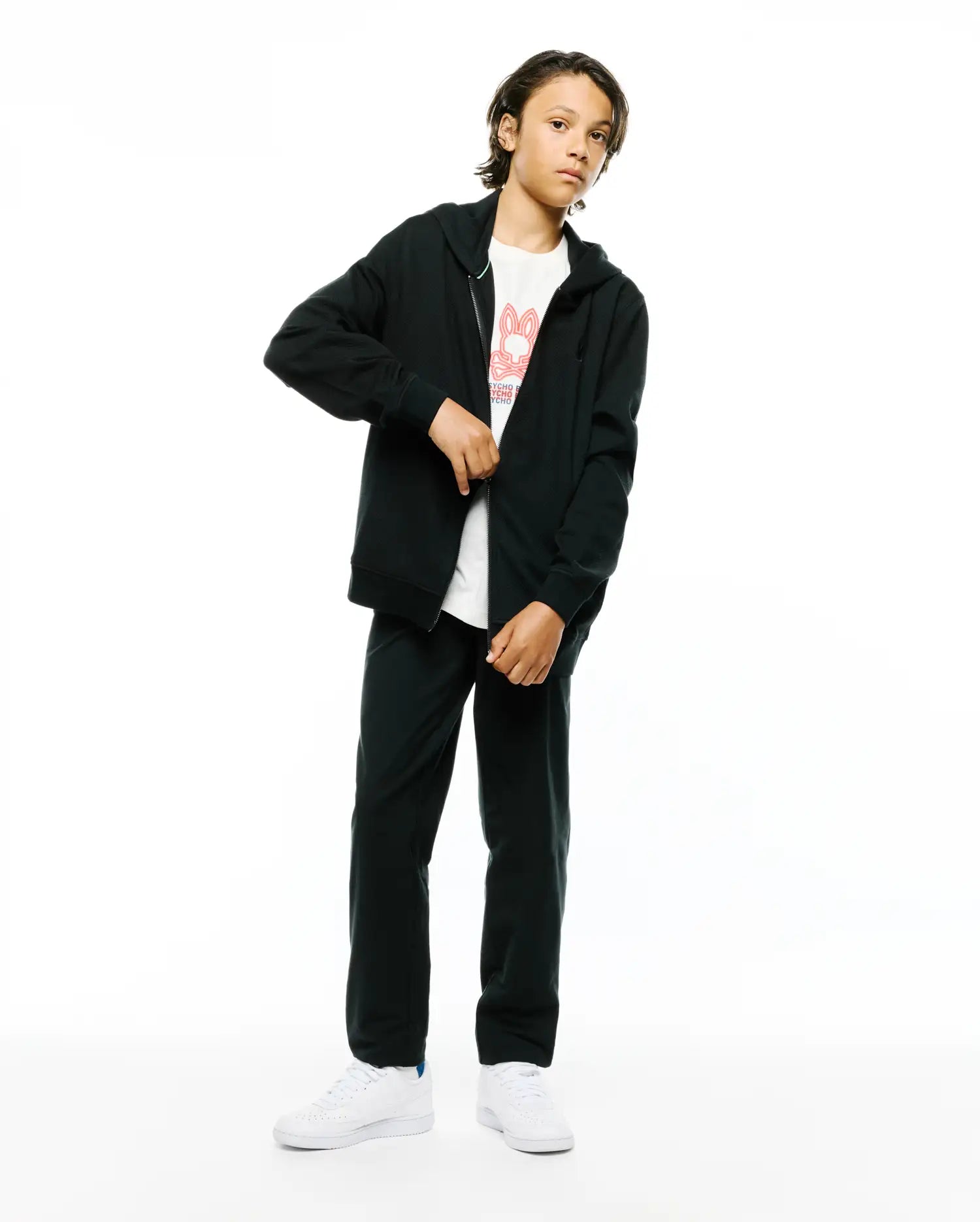 Kids Marc Textured Full Zip Hoodie in black, a relaxed-fit textured knit with silver zipper, layered over a white jersey tee featuring a large red Psycho Bunny skull logo and text, with matching black relaxed-fit sweatpants.