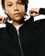 Kids Marc Textured Full Zip Hoodie in black, featuring a subtle textured pique fabric, a small tonal embroidered Psycho Bunny skull logo on the left chest, and a metallic zipper with a branded bunny skull pull.
