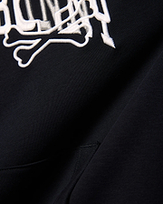 Kids Nathaniel Relaxed Hoodie in black, crafted from soft French terry, showcasing a prominent white embroidered Psycho Bunny skull and crossbones logo for a relaxed fit.