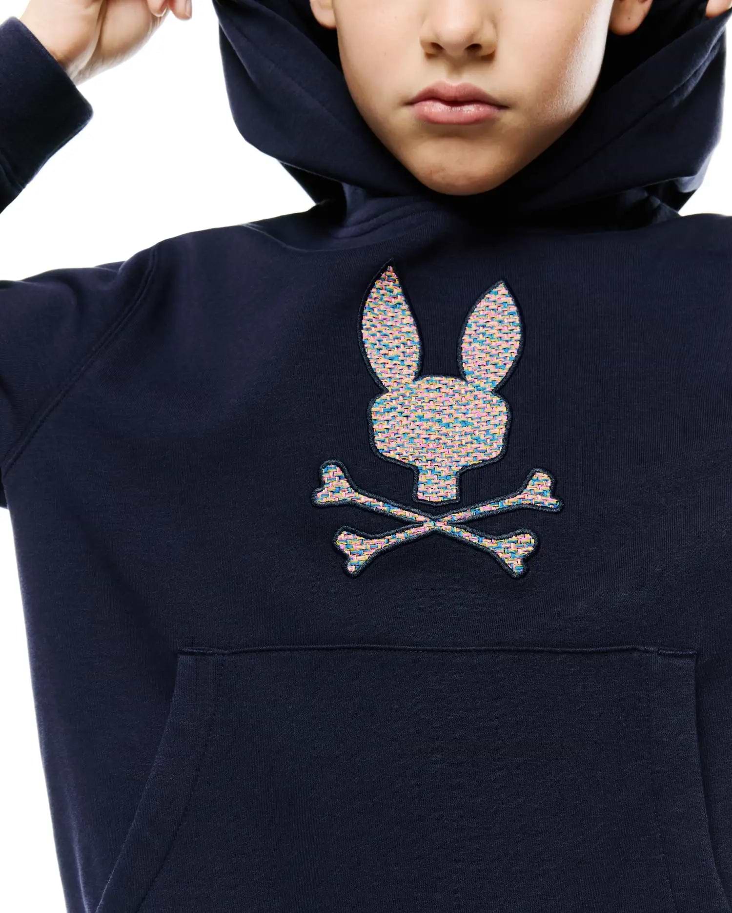 Kids Darcy Hoodie, a navy relaxed fit french terry hoodie with a large, center chest embroidered Psycho Bunny skull logo featuring a vibrant multicolored, textured weave and a front kangaroo pocket.