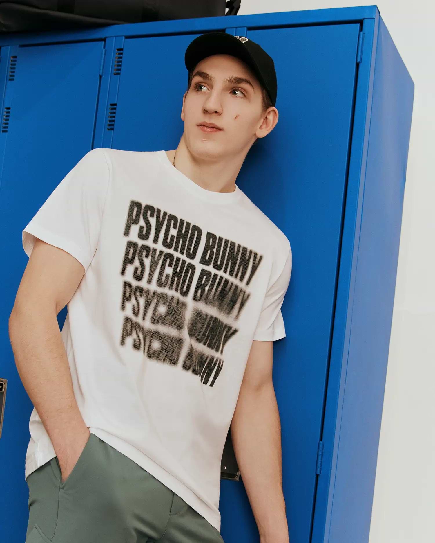 Mens Lawrence Graphic Tee, white classic fit smooth jersey knit t-shirt featuring a large, bold black blurred Psycho Bunny text graphic across the chest. (1)