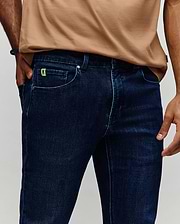 Mens Emerson Denim Pant, dark blue classic fit denim with light blue contrast stitching, featuring a small neon green embroidered Psycho Bunny skull logo on the coin pocket.