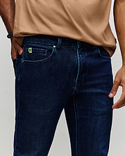 Mens Emerson Denim Pant, dark blue classic fit denim with light blue contrast stitching, featuring a small neon green embroidered Psycho Bunny skull logo on the coin pocket.