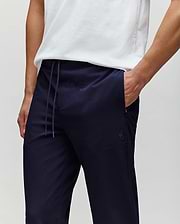A person models Psycho Bunny’s MENS BEN TECH JOGGER PULL ON - MB0600013 in dark navy polyester spandex, shown from shoulders to mid-thigh with one hand in their pocket against a plain background. (2)