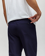 A man in a white shirt and PSYCHO BUNNY MENS BEN TECH JOGGER PULL ON pants (MB0600013) made from woven fabric stands with his back to the camera, pulling his shirt to show the "Psycho Bunny" logo above the back pocket. (3)