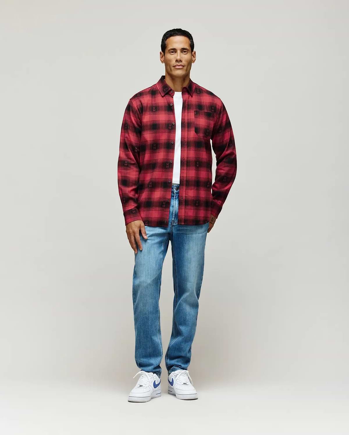 Red and black plaid flannel shirt, classic fit, featuring an all-over subtle Psycho Bunny skull pattern, layered over a white jersey t-shirt, and paired with light wash Mens Emerson Denim Pant.