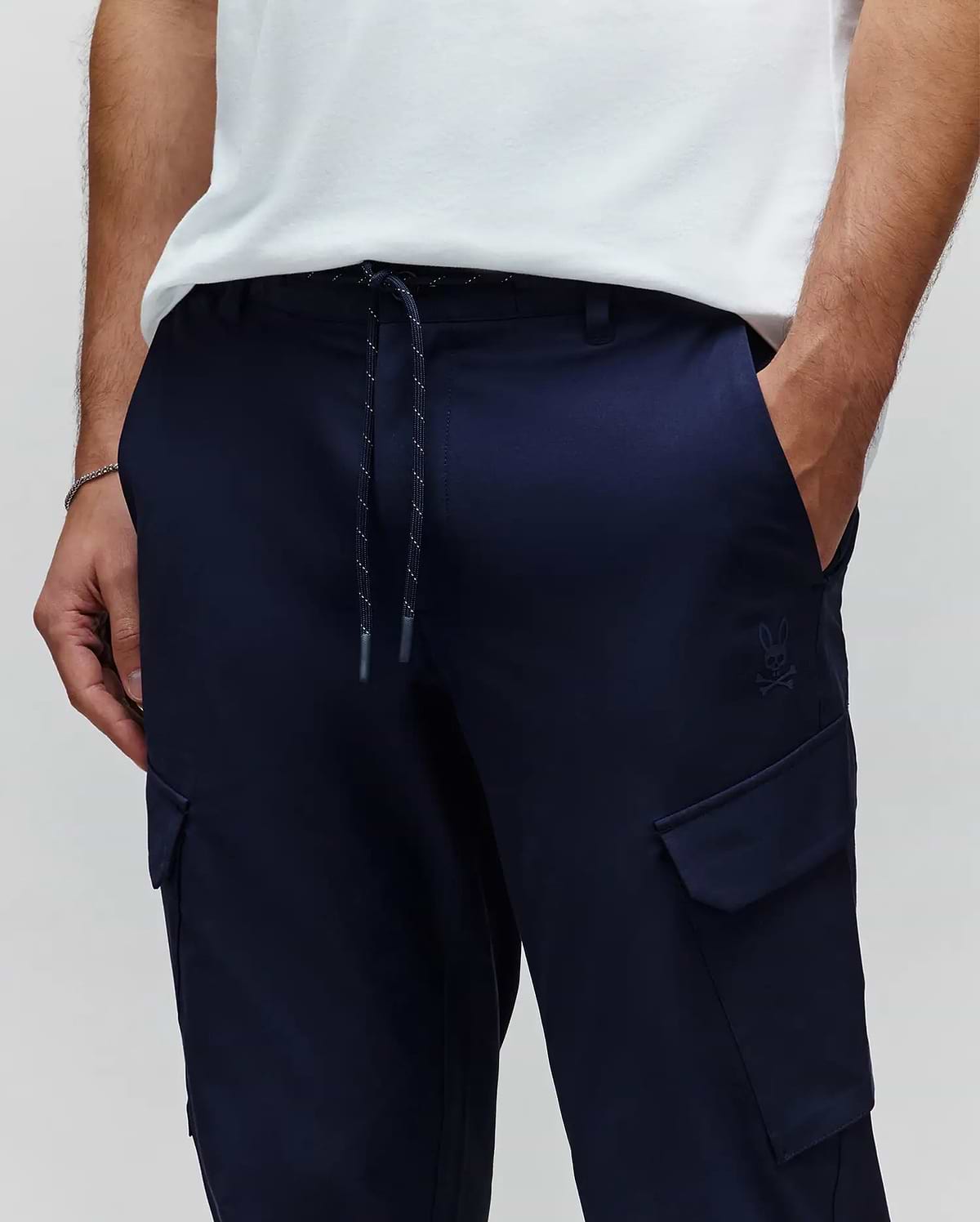 Mens Luka Cargo Pant in navy, featuring a relaxed fit, smooth fabric, drawstring waist with flecked cord, and a small tonal embroidered Psycho Bunny skull logo above the right cargo pocket. (2)