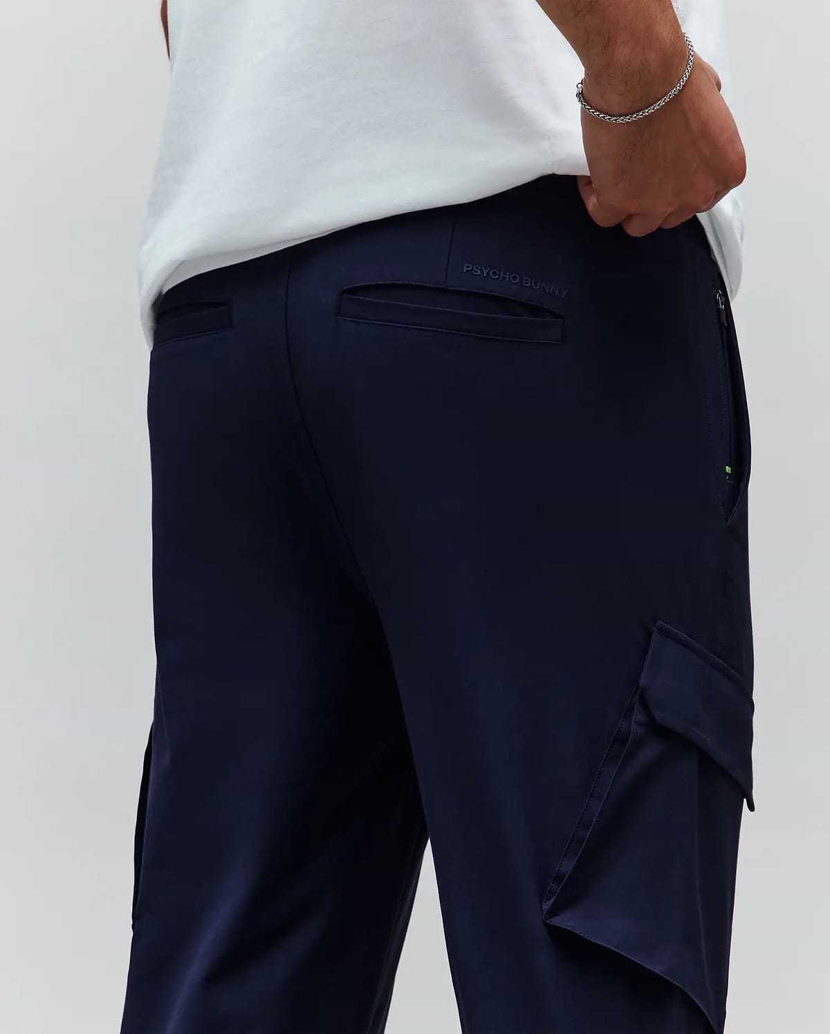 Mens Luka Cargo Pant in navy blue, featuring a relaxed fit, smooth fabric, side cargo pockets, back welt pockets, a small green accent on the side zipper, and an embroidered Psycho Bunny text logo on the back waistband. (3)