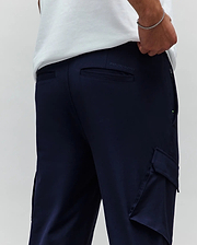Mens Luka Cargo Pant in navy blue, featuring a relaxed fit, smooth fabric, side cargo pockets, back welt pockets, a small green accent on the side zipper, and an embroidered Psycho Bunny text logo on the back waistband. (3)