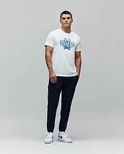 White jersey t-shirt with a large blue gradient Psycho Bunny skull graphic on the chest, paired with navy Mens Luka Cargo Pant featuring side pockets and a tapered fit. (5)