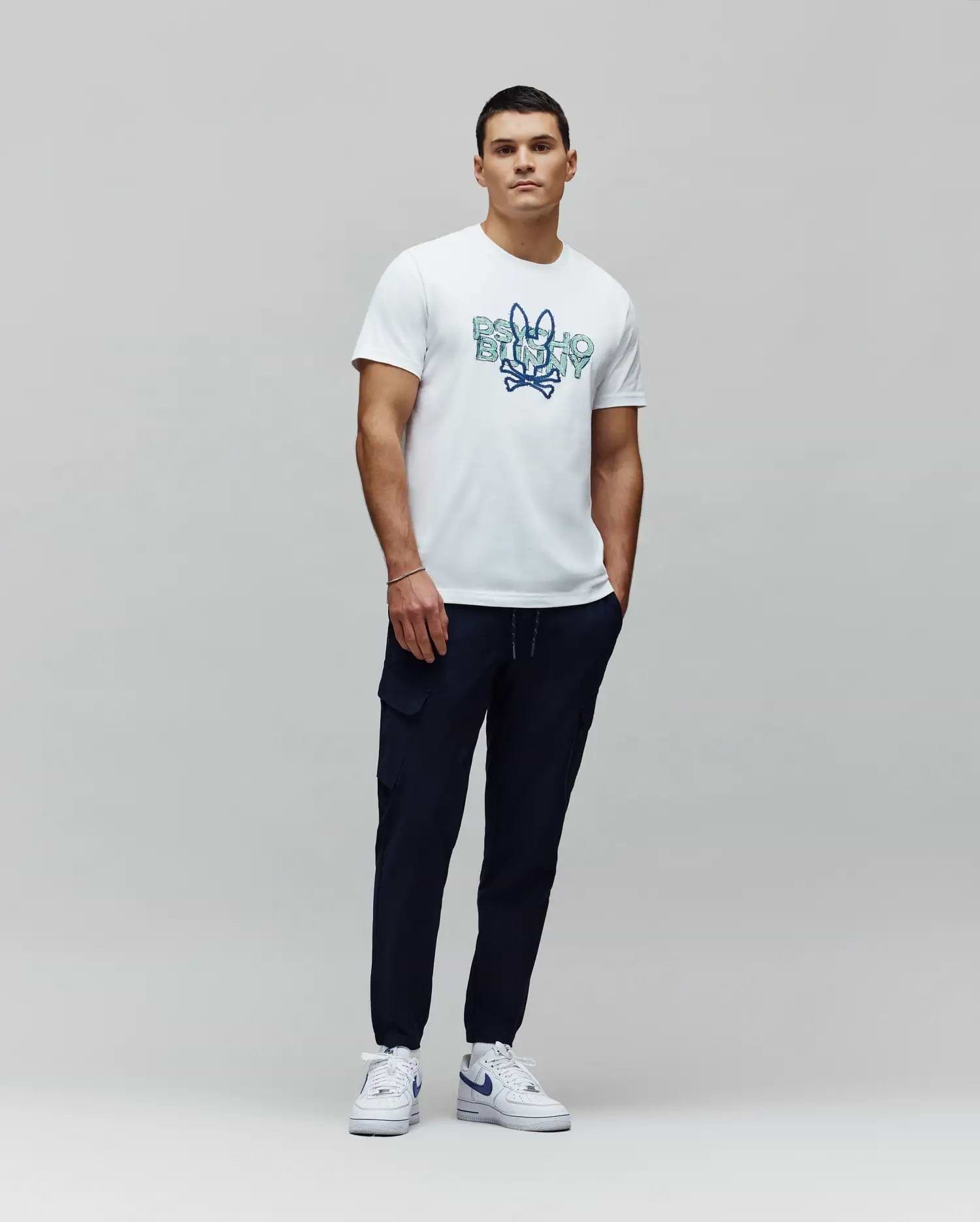 White jersey t-shirt with a large blue gradient Psycho Bunny skull graphic on the chest, paired with navy Mens Luka Cargo Pant featuring side pockets and a tapered fit. (5)