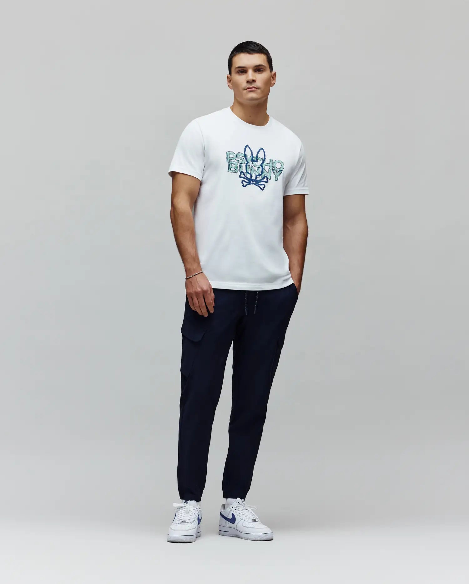 White jersey t-shirt with a large blue gradient Psycho Bunny skull graphic on the chest, paired with navy Mens Luka Cargo Pant featuring side pockets and a tapered fit. (5)