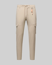 Mens Luka Cargo Pant in beige, featuring a relaxed fit, smooth fabric, side cargo pockets, and an elastic drawstring waist with an attached orange Psycho Bunny skull logo keychain.