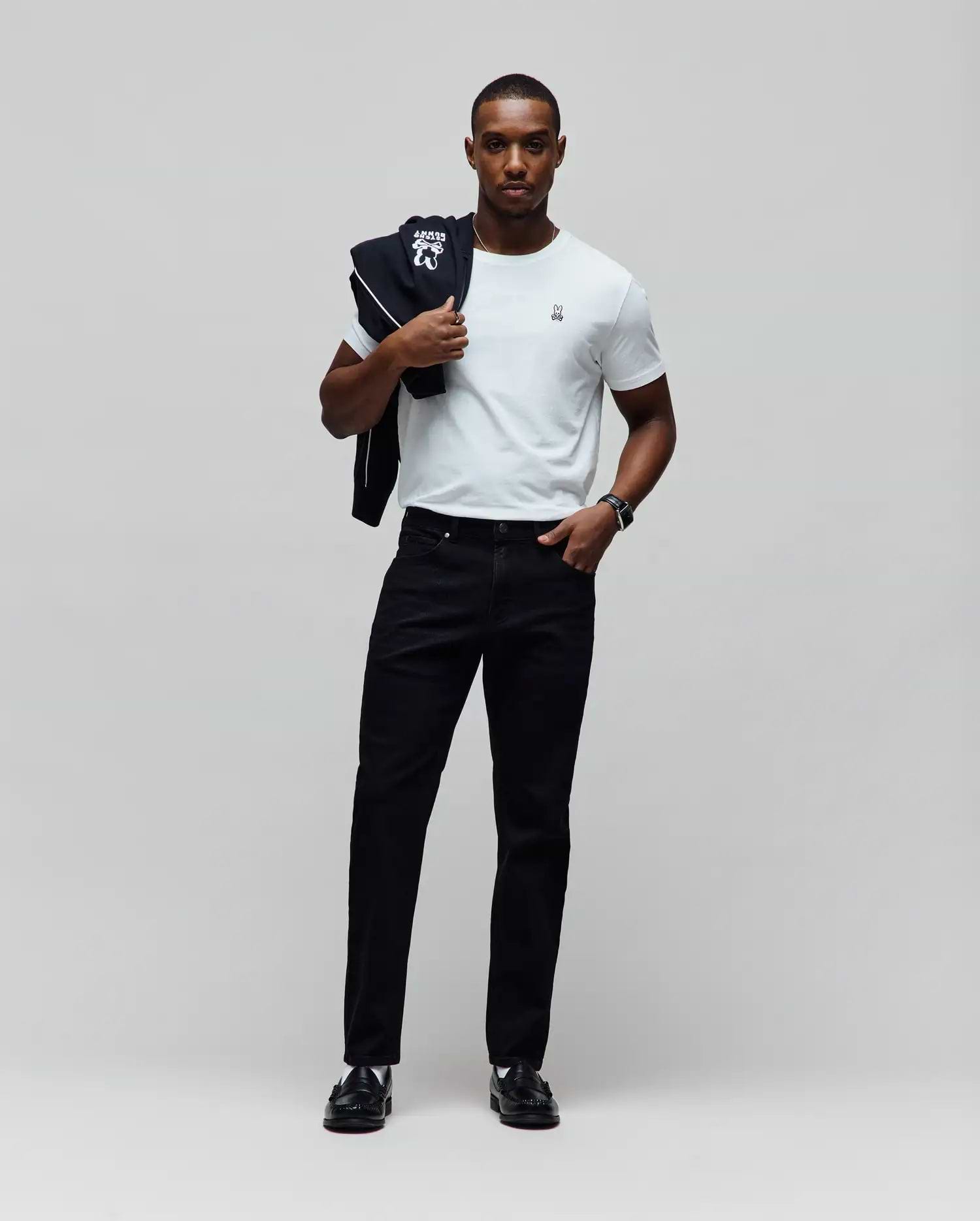 White jersey t-shirt with small embroidered Psycho Bunny logo on left chest, paired with black Mens Emerson Slim Fit Denim Pant and a black track jacket with large white Psycho Bunny graphic over the shoulder. (5)