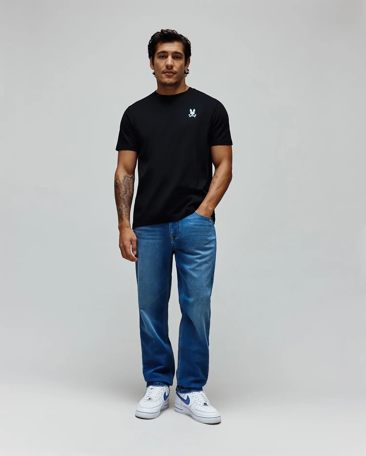 Black classic fit jersey t-shirt with small iridescent blue embroidered Psycho Bunny skull logo on left chest, paired with medium wash blue MENS ACE KNIT DENIM PANT. (5)