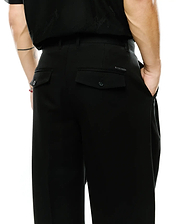 Men's Wayde Wide-Leg Pleated Pants in black, featuring a smooth fabric, wide-leg fit, two rear flap pockets with buttons, and a small metal Psycho Bunny logo tag above the right pocket. (3)