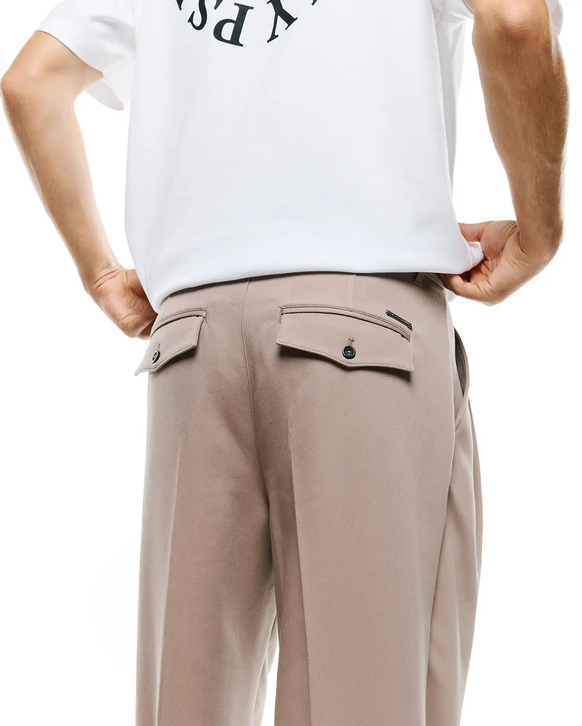 Men's Wayde Wide-Leg Pleated Pants in light beige, featuring back flap pockets with dark buttons and a small black brand tag, paired with a white relaxed-fit jersey t-shirt with a partial dark graphic print. (3)