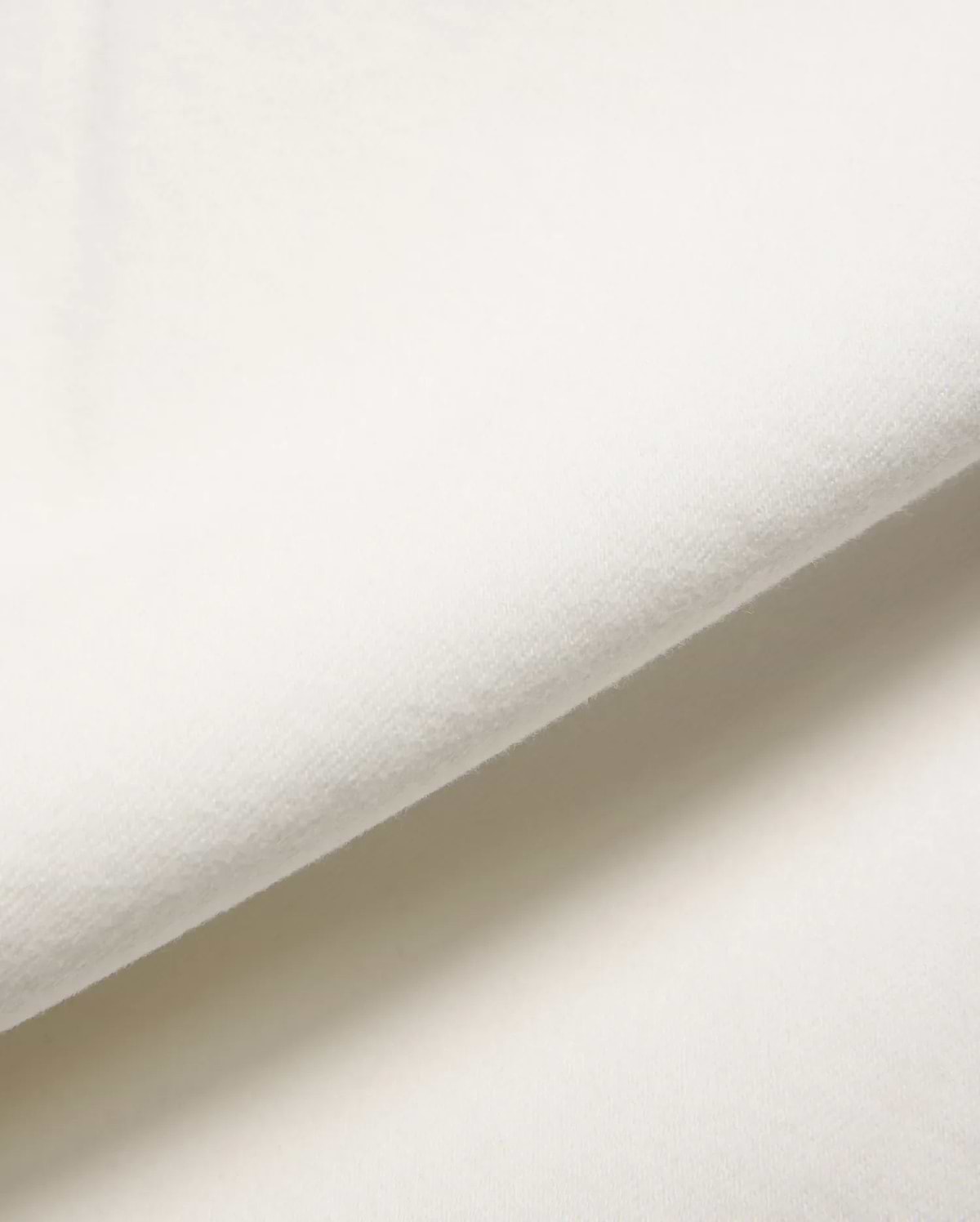 Mens Emerson Denim Pant in a crisp, creamy white, showcasing a premium, soft-touch denim fabric with a subtle, refined twill weave, gently folded to reveal its luxurious texture.