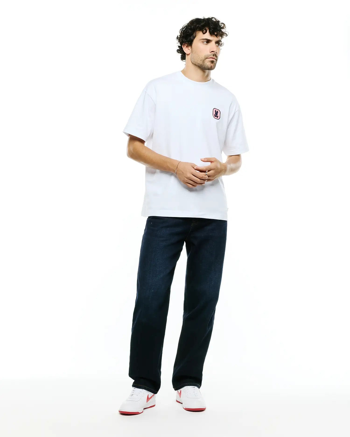 White relaxed fit jersey t-shirt with a small pink-outlined embroidered Psycho Bunny skull logo on the left chest, paired with dark indigo Men's Beck Oversized Denim Pants. (4)