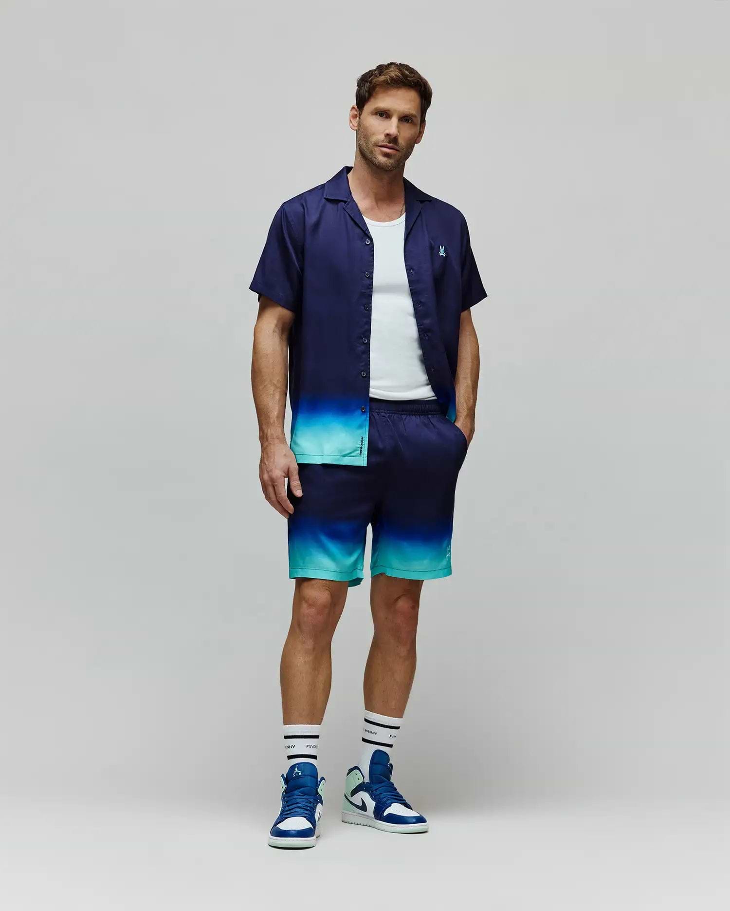 Relaxed fit navy short-sleeve button-up shirt and Mens Dax Tencel Short, with a vibrant blue and teal ombre fade. Shirt has a small embroidered Psycho Bunny skull logo, shorts include Psycho Bunny branding.