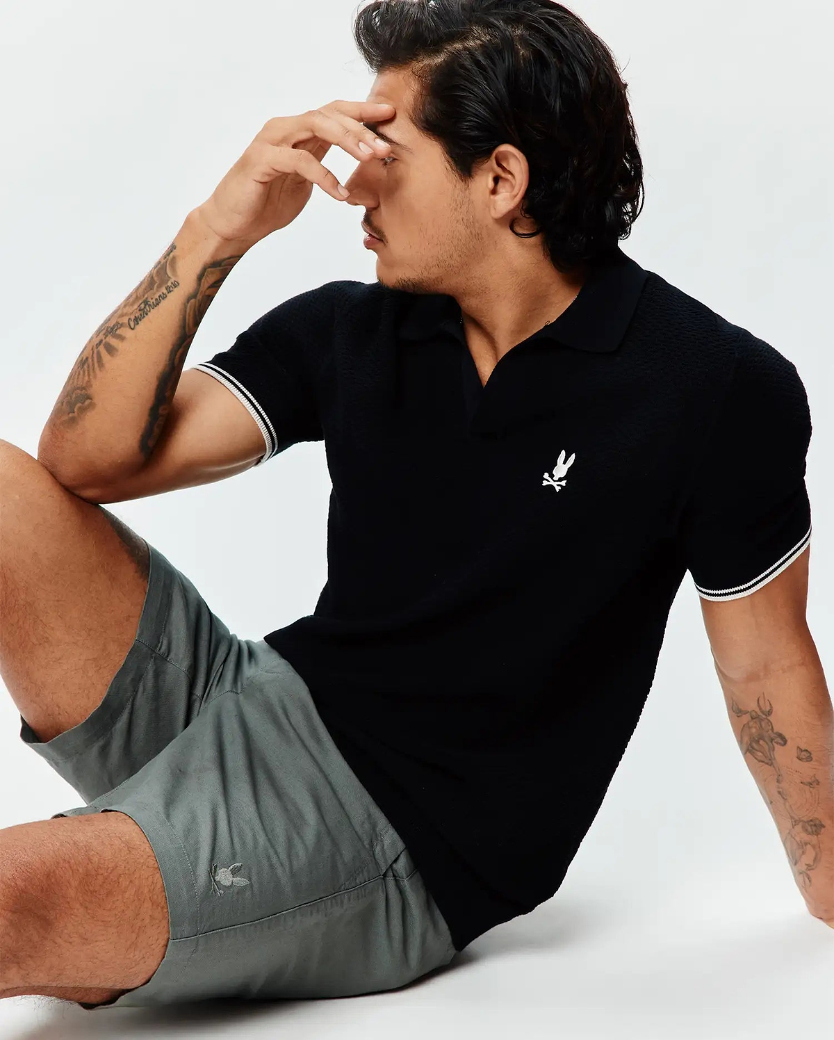 Black pique knit polo with white striped cuffs and an embroidered white Psycho Bunny logo on the chest, paired with Mens Ivan Linen Short in grey featuring a subtle embroidered grey Psycho Bunny logo on the leg.